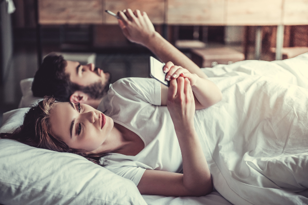 Junges Paar im Bett mit Handys - Ist das Handy am Bett schädlich?