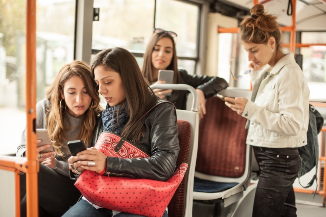 Junge Frauen im Bus, alle benutzen ein Handy - Mobilfunkstrahlung im Alltag reduzieren hilft der Gesundheit